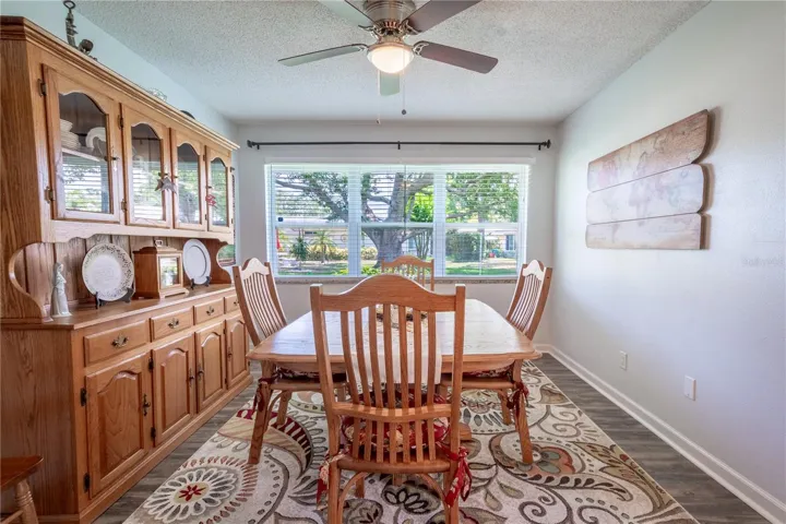 The dining room features wood plank vinyl flooring, a ceiling fan with light lit and a neutral color palette.