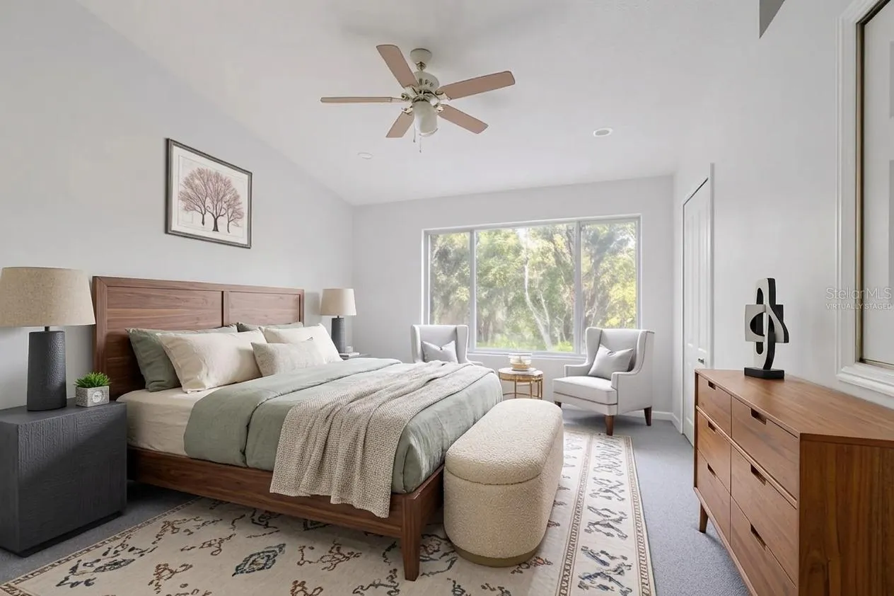 The Primary bedroom  features neutral tone walls and carpet, a ceiling fan with light kit and vaulted ceiling. (Photo has been virtually staged.)