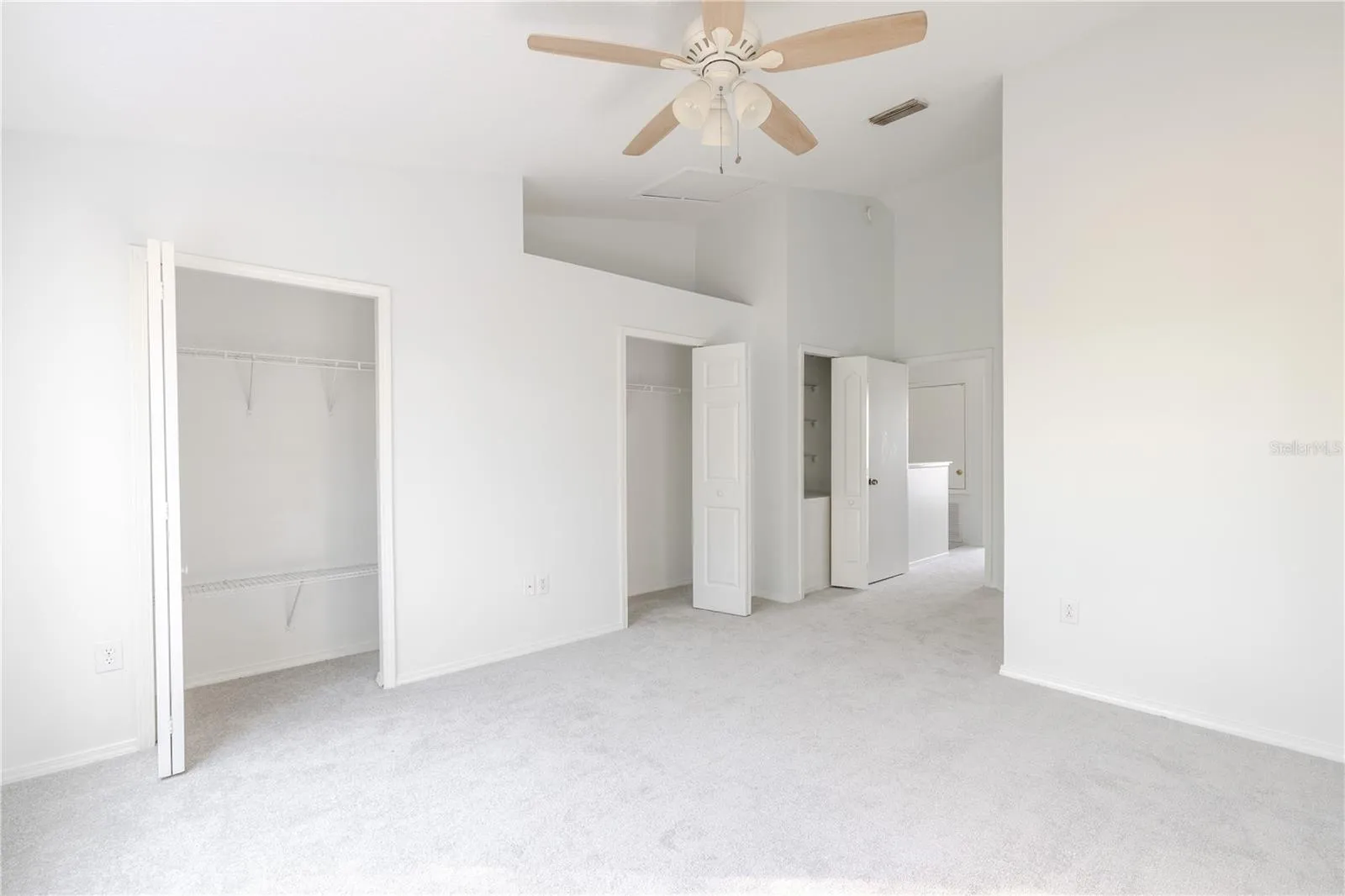 The Primary bedroom  features neutral tone walls and carpet, a ceiling fan with light kit and vaulted ceiling.