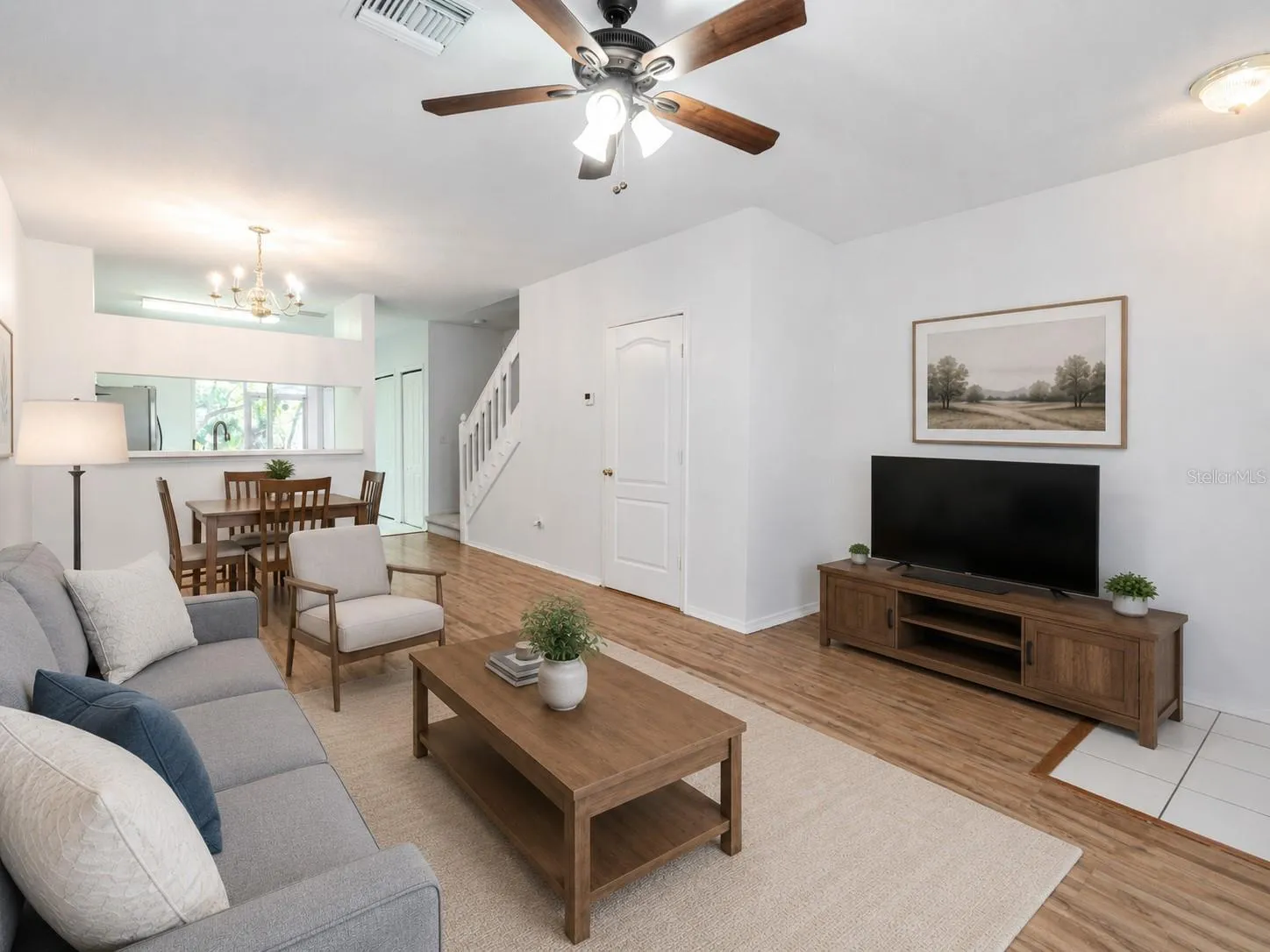 The Living room features neutral tones, wood laminate flooring, a ceiling fan with light kit and picture window.