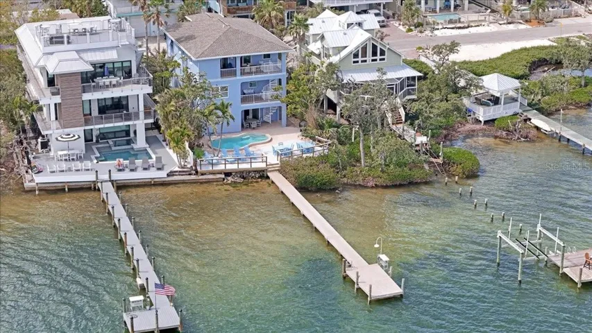 Aerial of blue home, large deck with pool area, and dock.