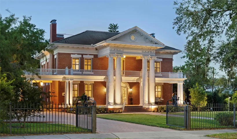 Stately Colonial Revival architecture distinguishes this luxury home for sale in Bartow, Florida, featuring red brick masonry, soaring Ionic columns, and a sweeping front porch on a landscaped corner lot.