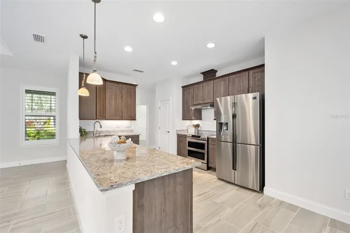 Kitchen with peninsula, mocha-colored cabinetry, recessed and pendant lighting