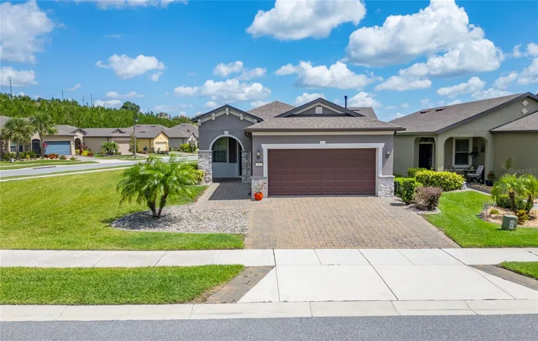 Front exterior of a Steel Creek model home on a corner lot in Del Webb Orlando, featuring a brick paver driveway in a 55+ gated community in Davenport, FL.