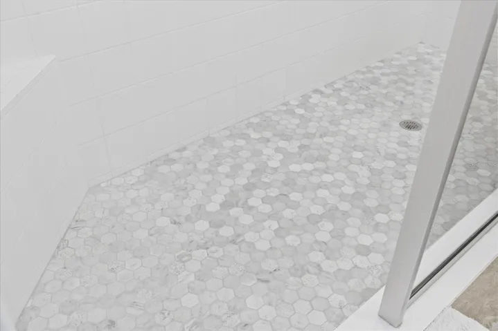 Corner shower seat and tiled shower floor with glass wall in primary bathroom