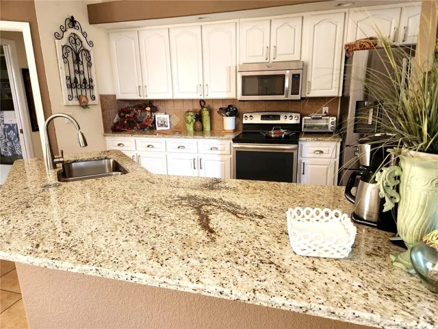 Bright, open kitchen featuring expansive granite countertops, white cabinetry, stainless steel appliances, and a large breakfast bar—perfect for entertaining and everyday living.