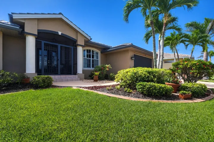 Inviting front entry framed by manicured landscaping and palm trees.
