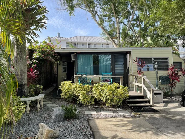 The staghorn fern hanging to the left near the palm tree will convey with the home. Low maintenance yard with river rock and concrete parking pad