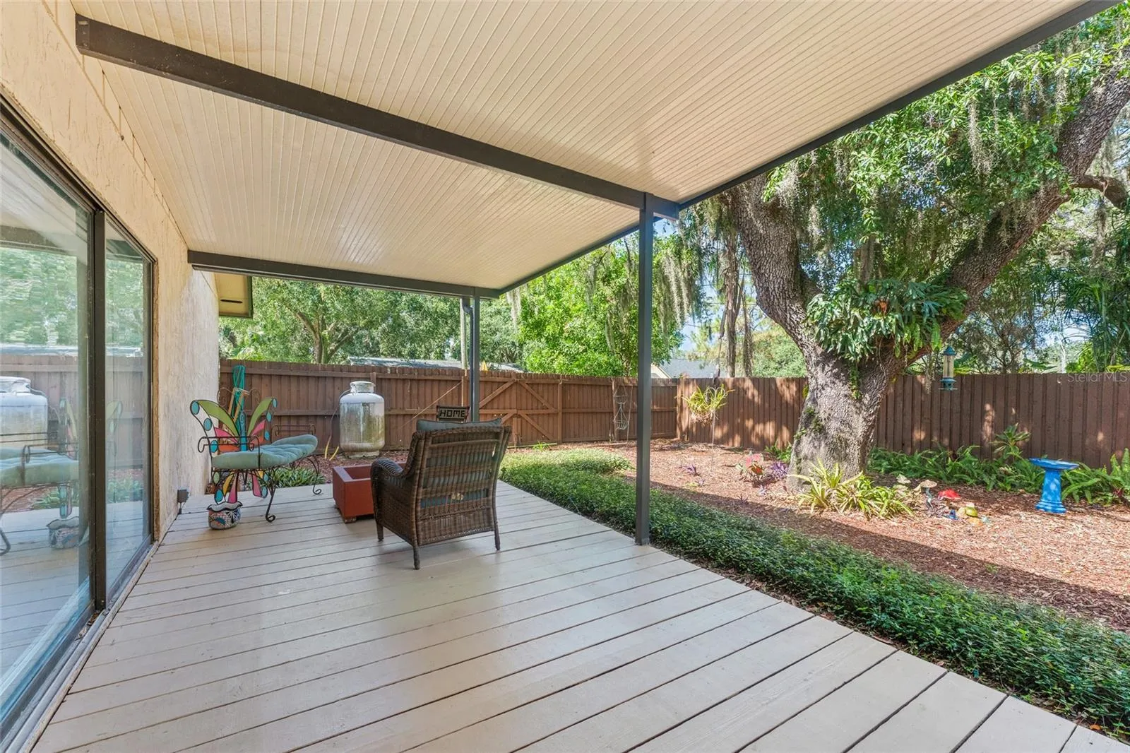 Backyard is surrounded by mature oaks, tropical landscaping, and a colorful garden.