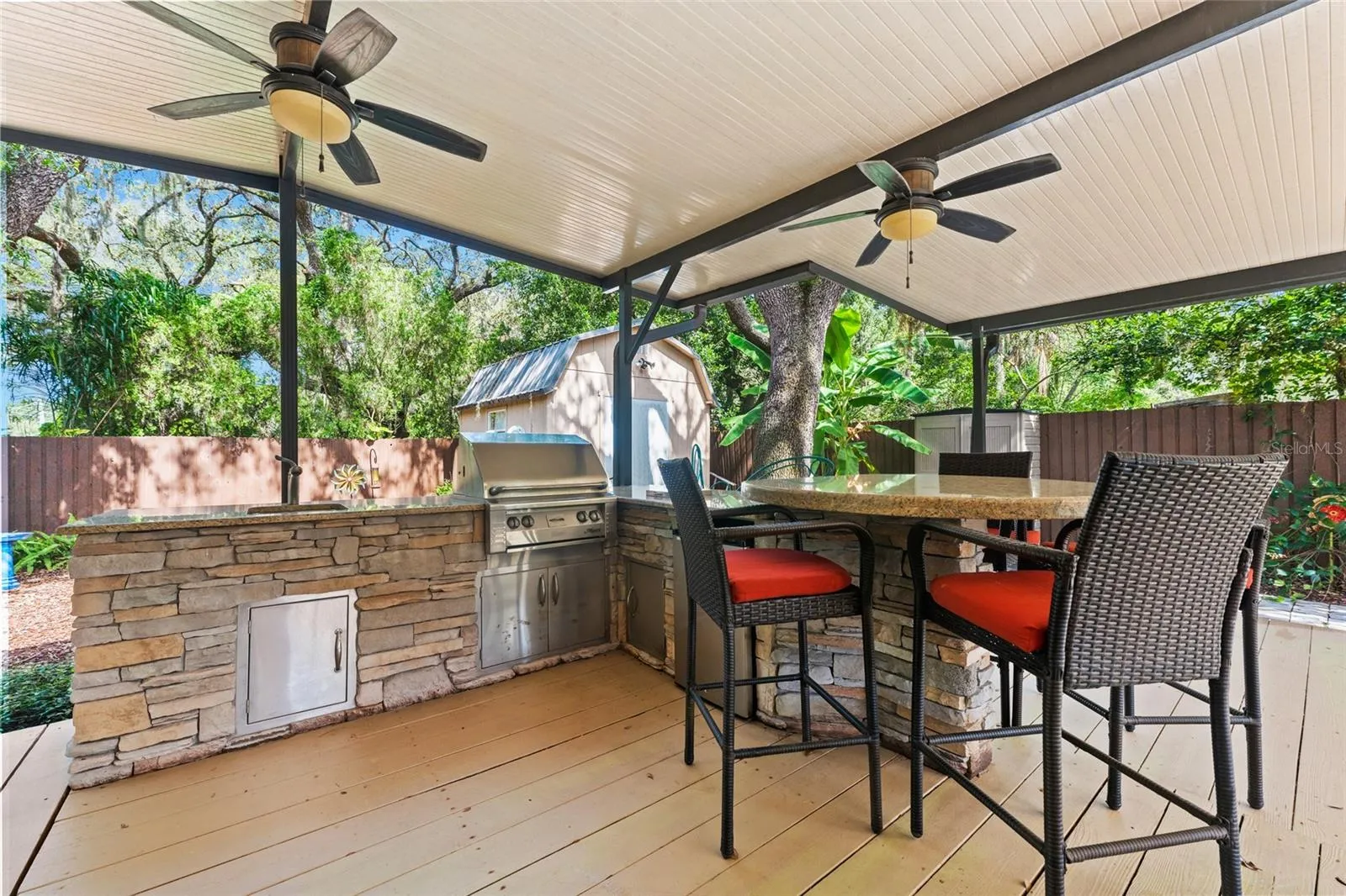 Outdoor Kitchen with a granite-topped bar, built-in gas grill, ceiling fans, and a gas fire pit.