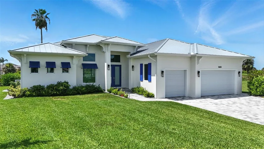 View of front facade featuring a garage, stucco siding, paver driveway, a front lawn, and a metal roof