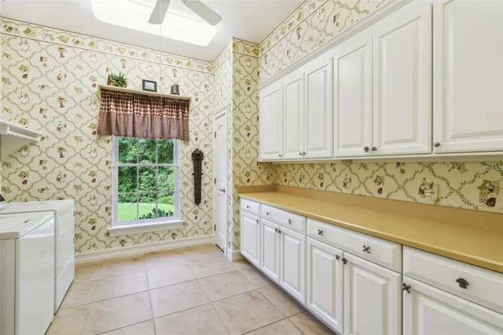 Well-appointed laundry room featuring a new washer and dryer, with a spacious folding counter, cabinets, and drawers spanning one wall. The opposite wall offers additional counter space and a utility sink. The room is plumbed for a gas dryer, though the current units are electric.