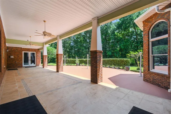 Expansive tiled lanai with ceiling fan, surrounded by mature hedges for privacy, and accessible from multiple rooms throughout the home.