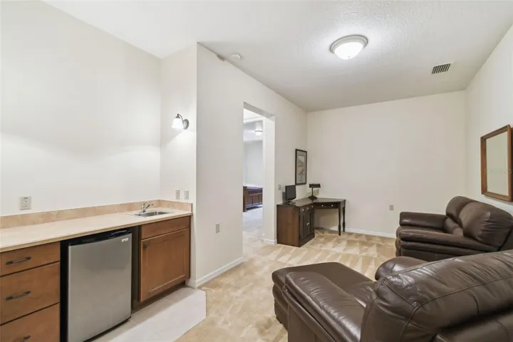 Upstairs features a spacious landing and inviting sitting room. Adjacent to the sitting area is a private guest suite with a connected full bathroom, along with an additional bedroom. The sitting room also includes a convenient kitchenette with a compact countertop, cabinet storage, sink, and mini refrigerator—perfect for guests or relaxing upstairs.