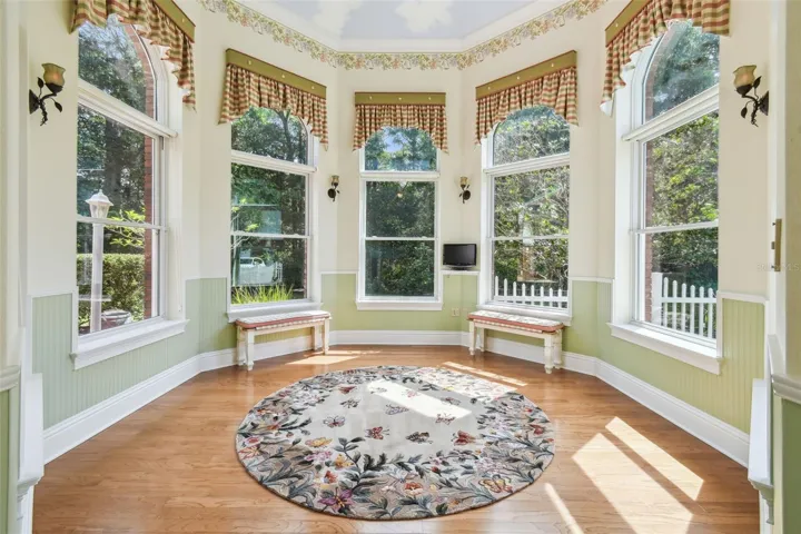 Charming garden room with a vaulted ceiling adorned with a sky mural and expansive panoramic windows that bring the outdoors in.