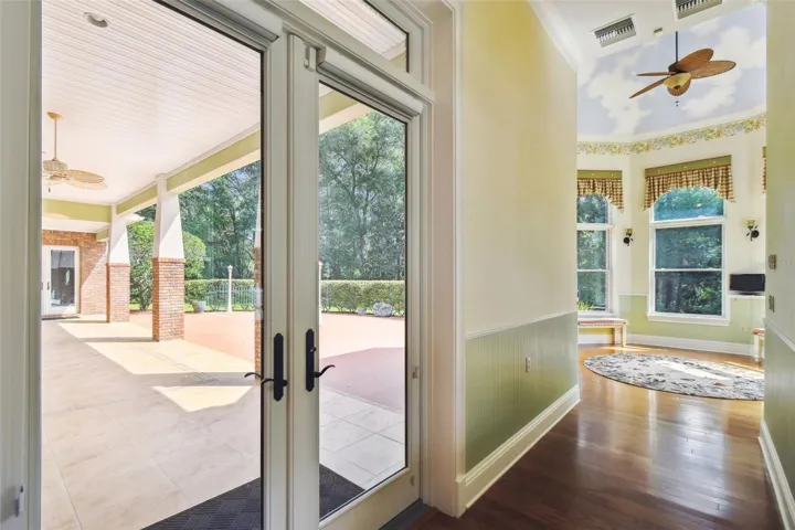 Expansive tiled lanai with ceiling fan, surrounded by mature hedges for privacy, and accessible from multiple rooms throughout the home.