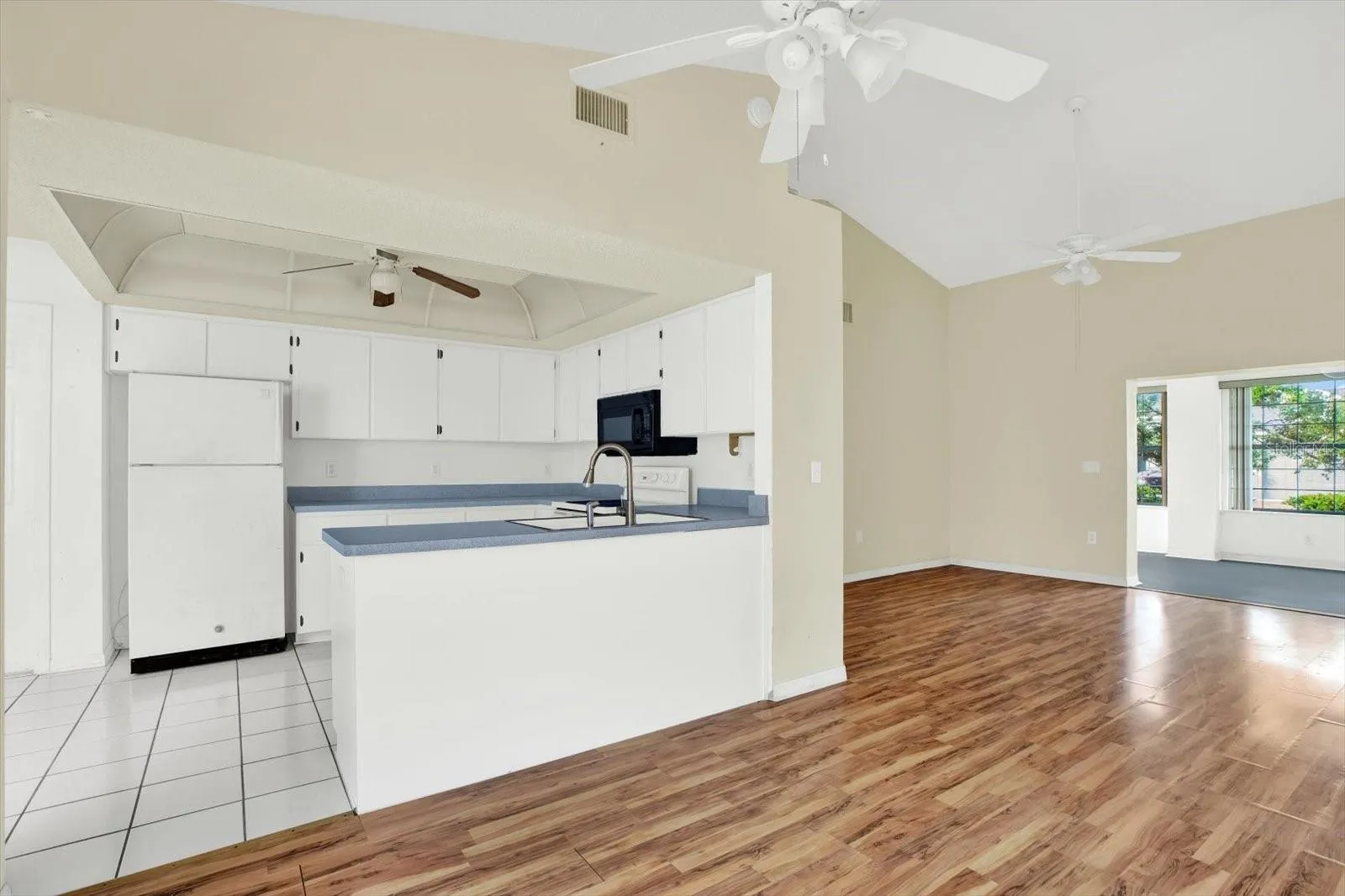 The kitchen, with white cabinets, tile flooring, and an open line of sight to the living room.