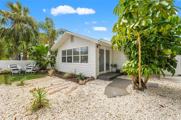Front Elevation – This charming 1925 bungalow makes a great first impression with tropical landscaping, a wide circular shell drive, and a private seating area nestled under mature palms.