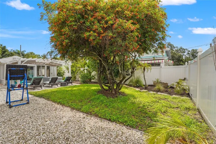 Relax + Play – This backyard is made for fun with a sunny lawn, lounging area, and even room for games like cornhole or target toss, all framed by tropical foliage and a white privacy fence.
