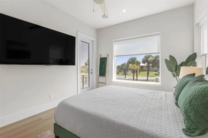 Framed by lush palm views, this comfortable guest bedroom boasts a peaceful ambiance, balcony access, and a mounted TV—ideal for relaxation after a day at the beach