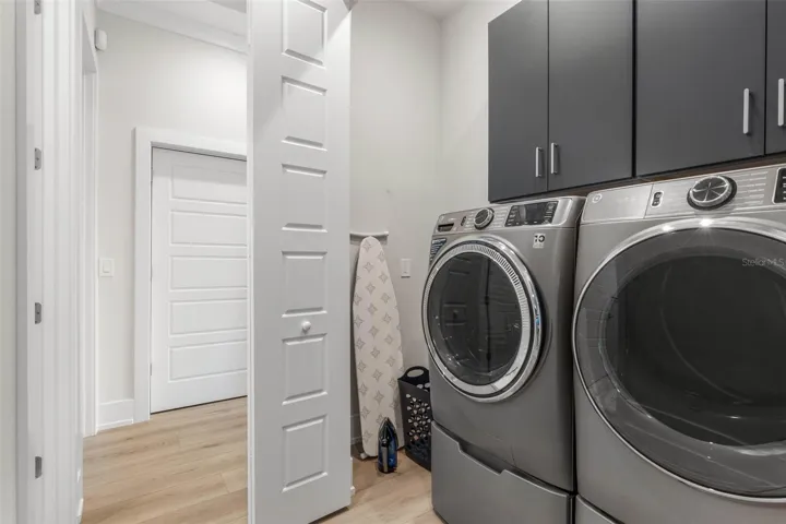 Tucked behind double doors, this sleek laundry area features modern front-load appliances, built-in cabinetry for extra storage.