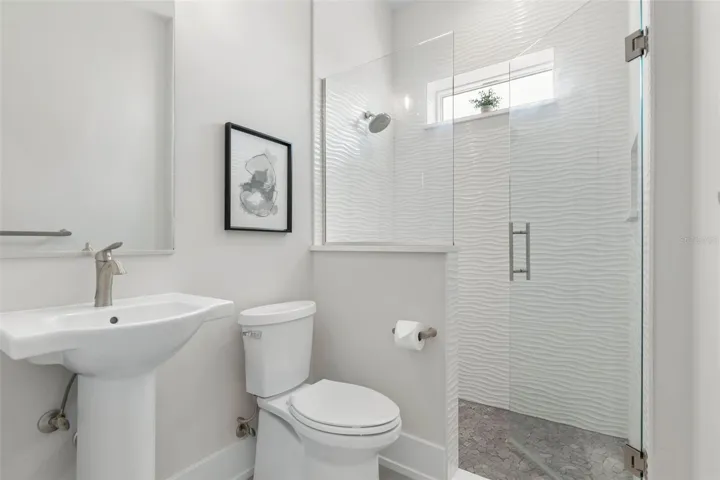 Bright and modern guest bath featuring textured wave tile, pebble stone shower flooring, a sleek frameless glass enclosure, and stylish brushed nickel finishes—where spa vibes meet everyday function.