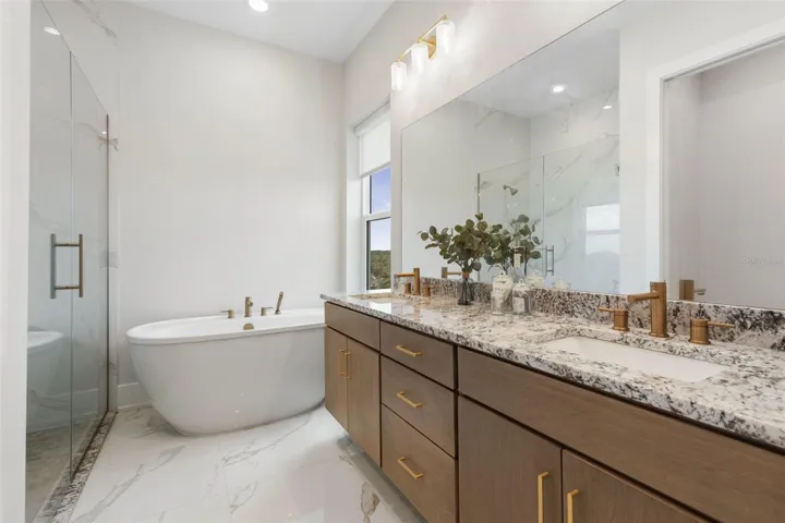 The spa-inspired ensuite features a luxurious soaking tub, glass-enclosed shower, dual vanities with granite countertops, and elegant gold-tone fixtures throughout.