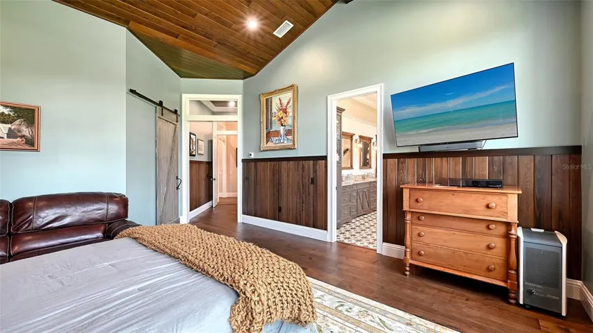 Primary Suite #1 boasts breathtaking vaulted ceilings, elegantly enhanced by poplar-wrapped beams and #2 cypress V-joint tongue-and-groove. A stunning 48" chair rail complements the design, with an 8" T&G nickel gap FJ pine below. The tongue-and-groove (T&G) construction not only adds visual interest but also ensures a seamless fit between the boards, creating a polished and cohesive look. This technique allows for a snug connection that minimizes gaps, enhancing both the aesthetic appeal and structural integrity of the walls. The warm tones of the FJ pine further enrich the space, creating a cozy and inviting atmosphere in this serene retreat.