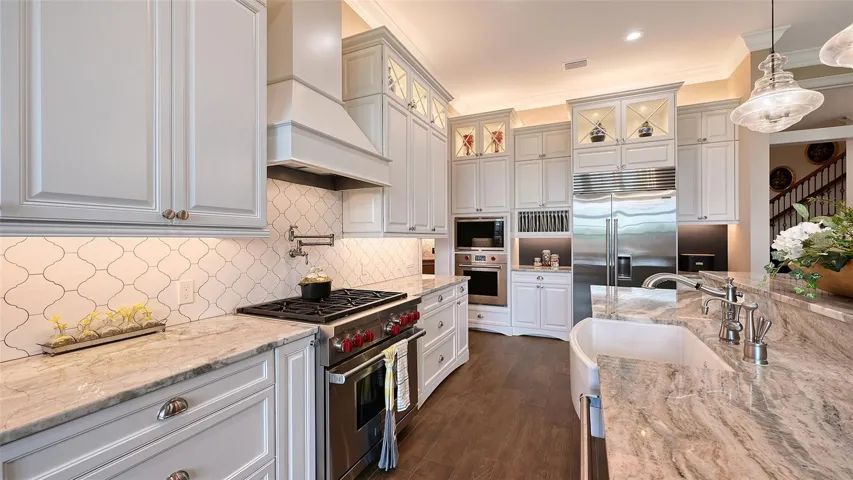 Custom-painted island cabinets and a bespoke range hood add a unique touch. The space is adorned with Level 5 granite countertops and a stylish tiled backsplash.