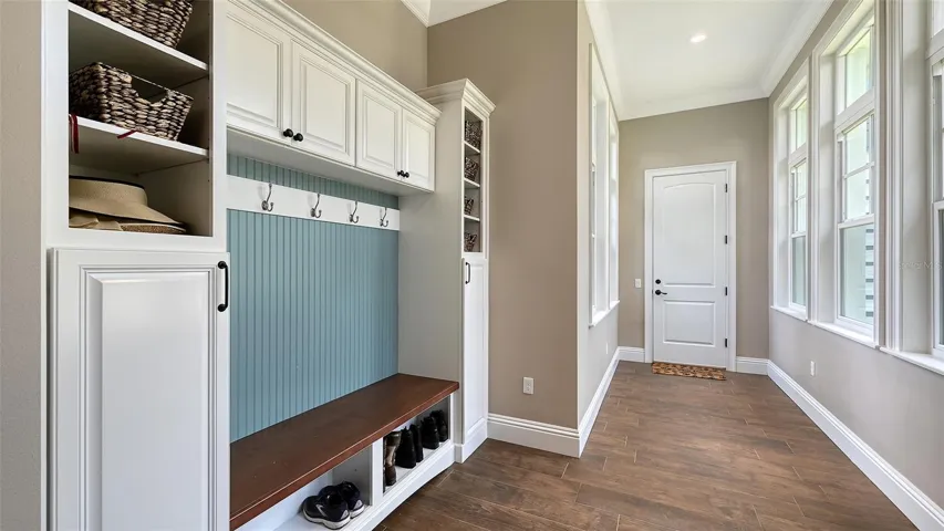 Step into the inviting mud room, conveniently located off the garage and measuring 10' x 14'. This functional space is flooded with natural light from windows on both sides of the hallway, creating a bright and welcoming atmosphere. Featuring custom built-ins, including a stylish bench with storage and hooks for coats and bags, this mud room is designed for both organization and convenience. Haven Barrel 8"x 40" porcelain tile flooring enhances the aesthetics of the room. This is the perfect transition space that combines practicality with charm, making it an essential part of your home!