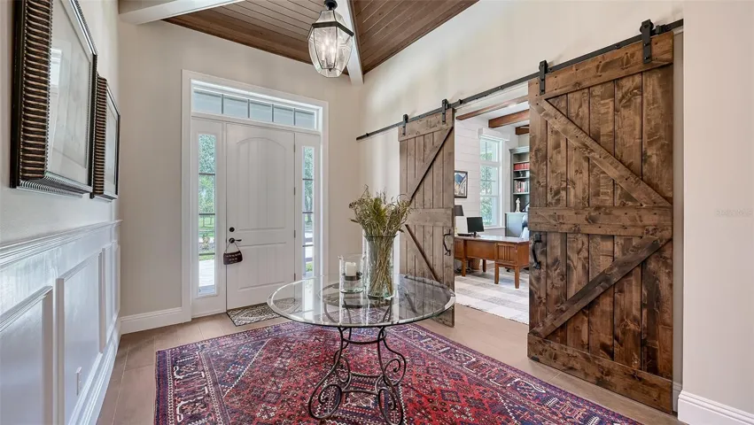 The stunning barn doors lead to a spacious study that boasts 12' ceilings and measures 16' x 13'. The door hardware features a Schlage Addison handle set with champagne levers and aged bronze finishes for both exterior and interior doors, ensuring a cohesive aesthetic throughout. The foyer showcases painted poplar-wrapped beams and #2 cypress V-joint tongue-and-groove (prefinished Synergy wood) in an elegant X design. The barn doors are crafted from Glass Craft Knotty Alder and accented with sleek black hardware, including models Slade BDAOIK, Monterey HP2, and Vista HP4, adding a touch of sophistication to the space.