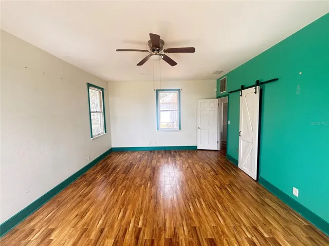 The second ensuite offers a spacious layout with beautiful wood flooring, abundant natural light, and charming architectural elements including sliding barn doors and multiple access points. While the room is generous in size and full of potential, the existing bold wall colors and minimal finishes leave the space feeling unfinished and ready for personalization