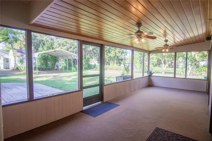 The screened in Patio with carpet and wood ceiling with ceiling fans.