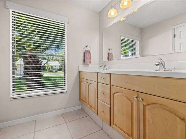THE PRIMARY BATHROOM HAS AN UPDATED DOUBLE SINK VANITY, CERAMIC TILE FLOOR, SOLID SURFACE COUNTERS