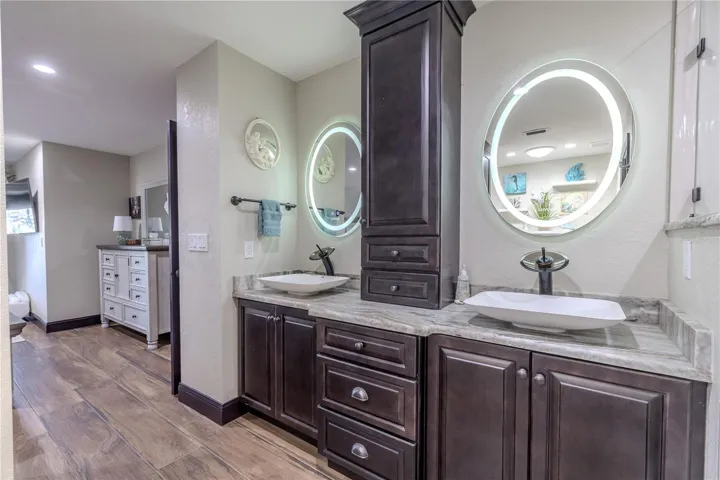 The primary bath showcases stunning split vanities with stone countertops, LED lighted mirrors, and custom water faucets chosen for their sleek and artistic design.