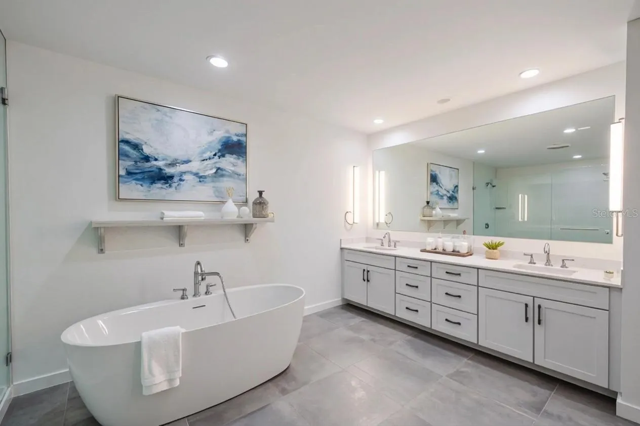 The primary bathroom features a sophisticated double vanity with an expansive quartz countertop, dual undermount sinks, and abundant drawer storage. Sleek brushed nickel hardware and soft-close cabinetry complement the clean, modern aesthetic. A full-width mirror framed by contemporary vertical sconces provides excellent lighting and adds to the spa-like ambiance of this beautifully designed space.