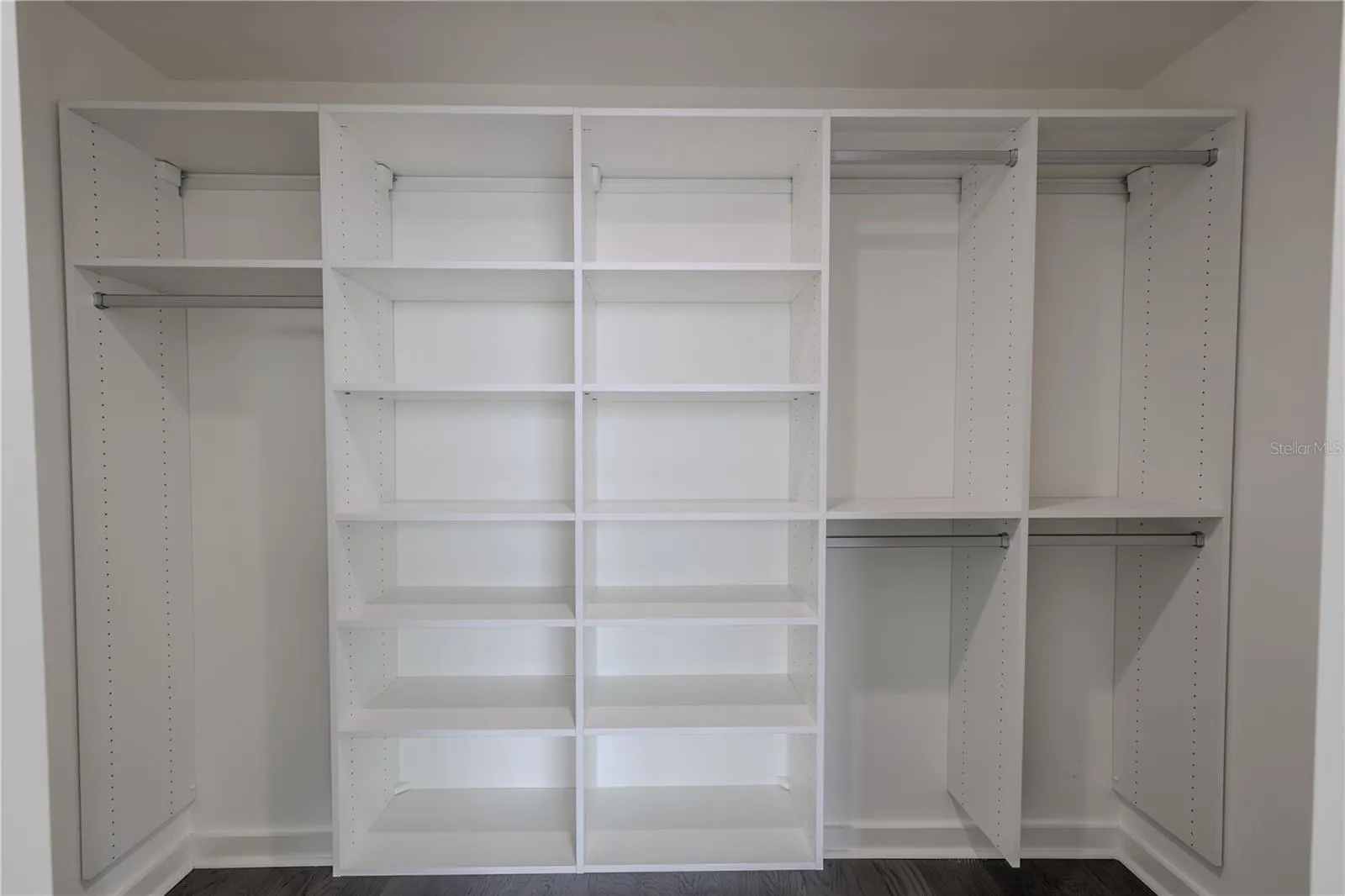 The spacious walk-in closet for Bedroom 2 offers exceptional organization with a custom built-in system featuring multiple open shelves and double hanging sections. Clean white finishes and adjustable shelving provide versatility for clothing, shoes, and accessories, while the streamlined layout maximizes storage and accessibility. Perfectly designed to complement the modern style of the suite, this closet delivers both form and function in a bright, polished space.