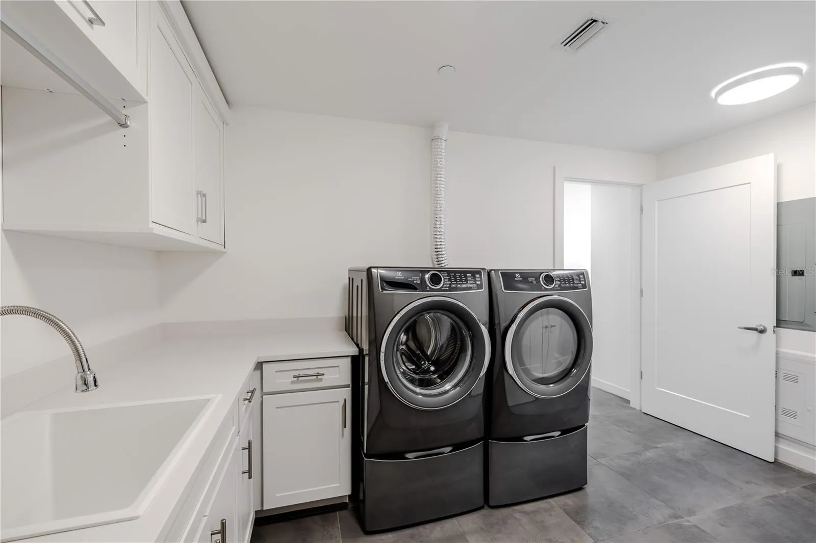 The beautifully designed laundry room features a sleek Electrolux front-load washer and dryer set, surrounded by abundant cabinetry and  countertops for folding and organization. A deep utility sink and hanging rack add everyday convenience, while modern tile flooring and recessed lighting create a clean, contemporary look. Practicality meets style in this thoughtfully planned space.