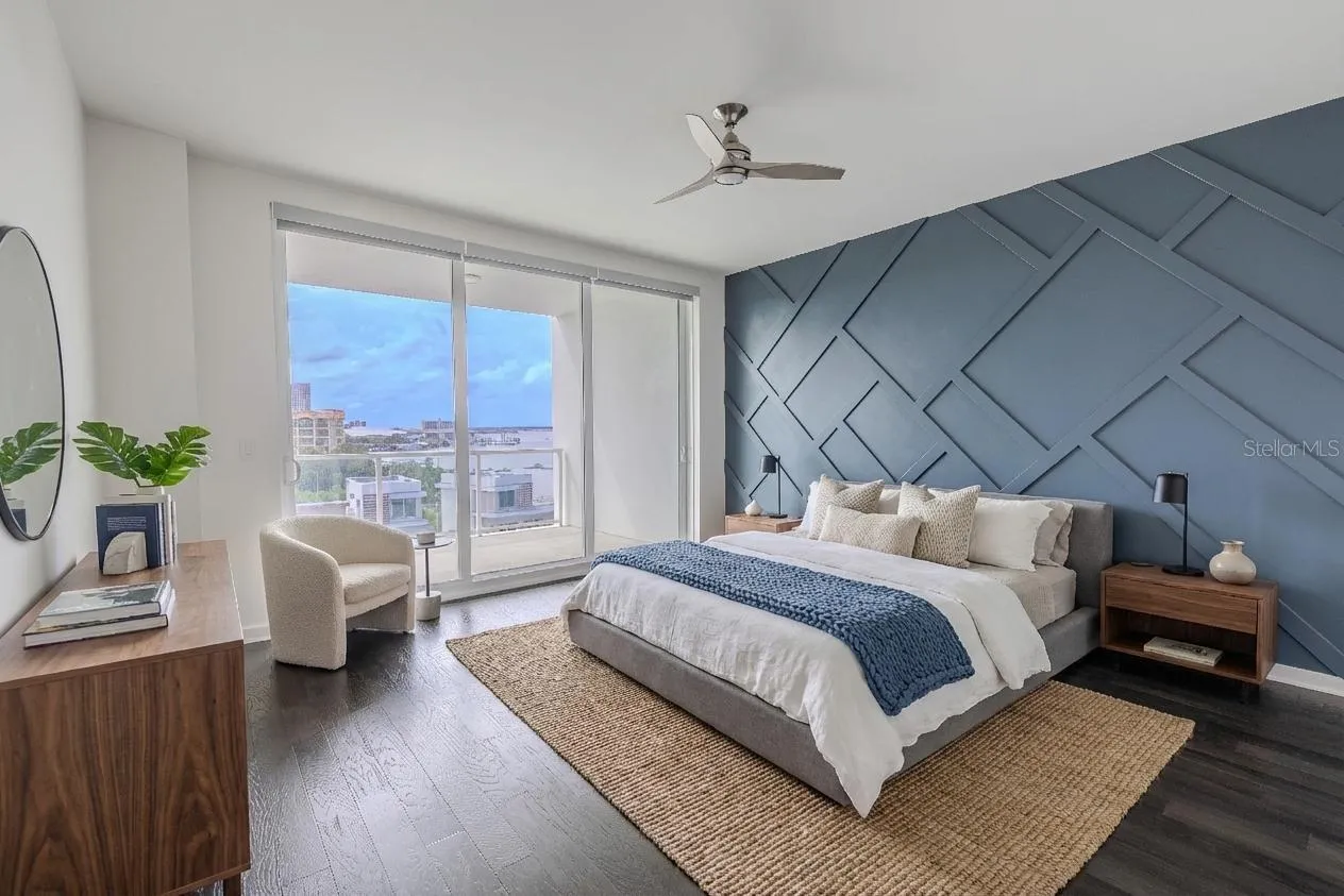 The primary bedroom features a striking custom accent wall that adds architectural depth and modern sophistication. Painted in a rich slate blue, the wall showcases a geometric grid pattern of raised molding, creating a dramatic focal point that complements the room’s sleek aesthetic. The textured design plays beautifully against the dark hardwood floors and natural light, offering the perfect balance of contemporary style and visual interest.