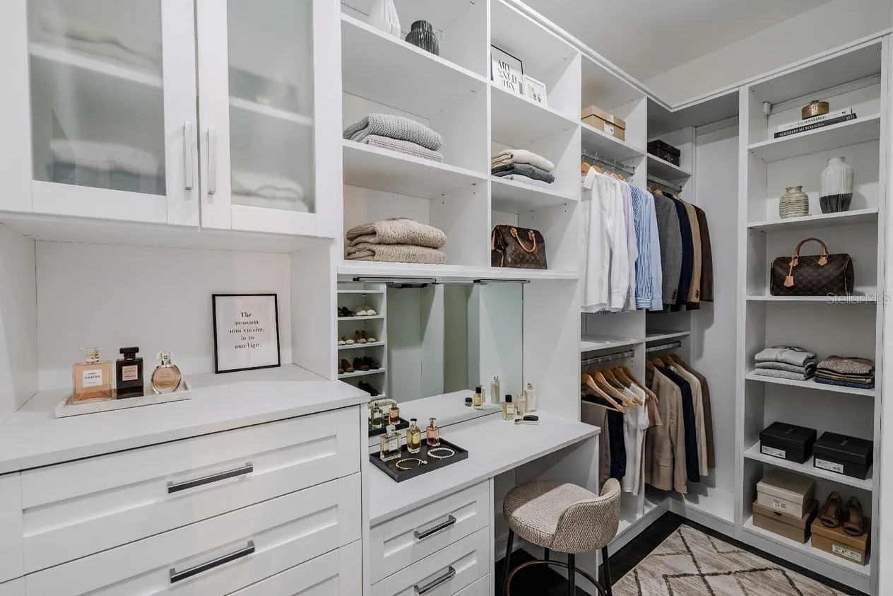The secondary primary closet offers exceptional organization and functionality, featuring custom built-ins with open shelving, drawers, and hanging space. Frosted glass cabinet doors add a touch of elegance, while a built-in vanity with mirror and ample countertop space provides a perfect spot for getting ready. Thoughtfully designed to maximize storage and style