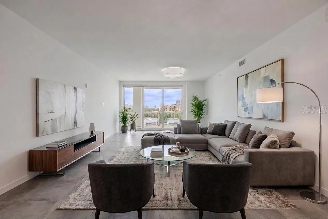 This bright and spacious dining and living area offers an elegant, open layout with sleek tile flooring and contemporary lighting. Floor-to-ceiling glass doors flood the space with natural light and open to a large balcony with sweeping water and skyline views. The modern chandelier adds a touch of sophistication, creating the perfect setting for entertaining or relaxing in style. Virtually staged photo.