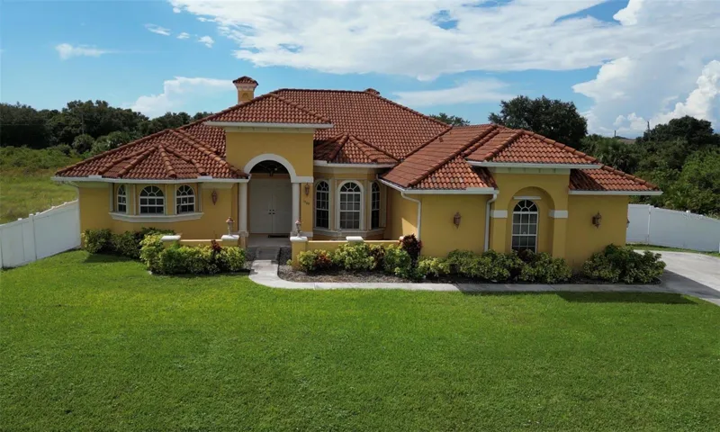 Mediterranean/Spanish style home featuring stucco siding and tiled roof with decorative chimney on half-acre lot with fully fenced yard.