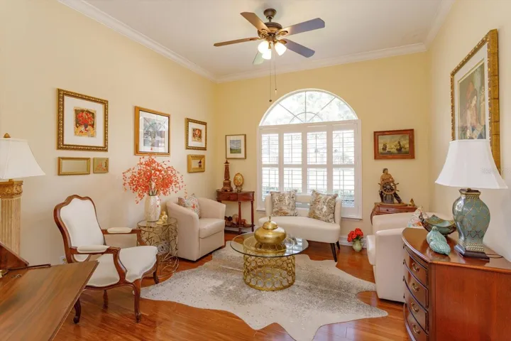 Lovely living room.  Crown molding, lighted ceiling fan, attractive flooring and natural light from sun burst window with shutters.