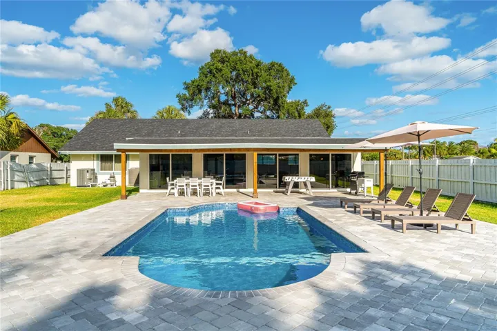 Resort-style backyard featuring a sparkling pool, spacious paver deck, covered patio, and ample lounge space—perfect for relaxing or entertaining.