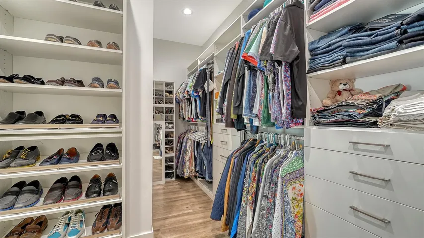 Primary bedroom walk-in closet with built in shelving, drawers, and shoe racks.