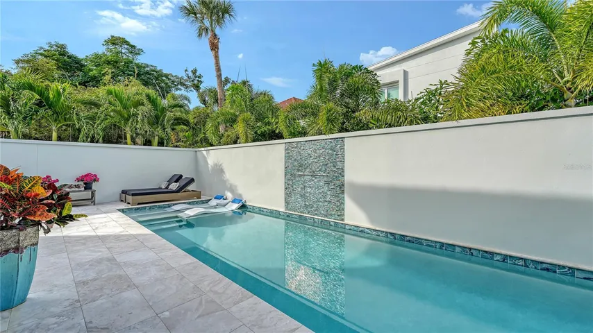 Pool and pool deck featuring marble deck, water fall and fountains. Colorful lighting at nightime.