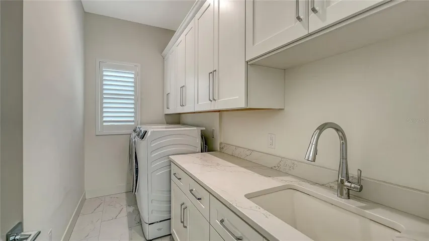 2nd floor laundry room with utility sink, granite countertop and custom wood cabinets for storage.