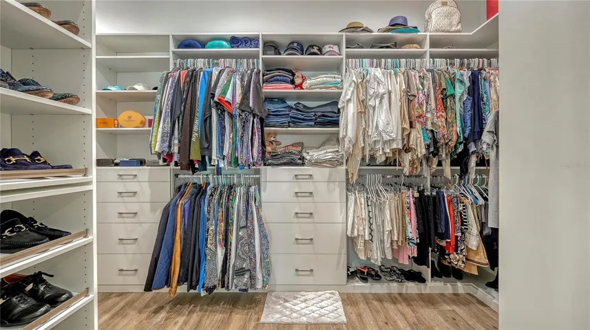 Primary bedroom walk-in closet with built in shelving, drawers, and shoe racks.