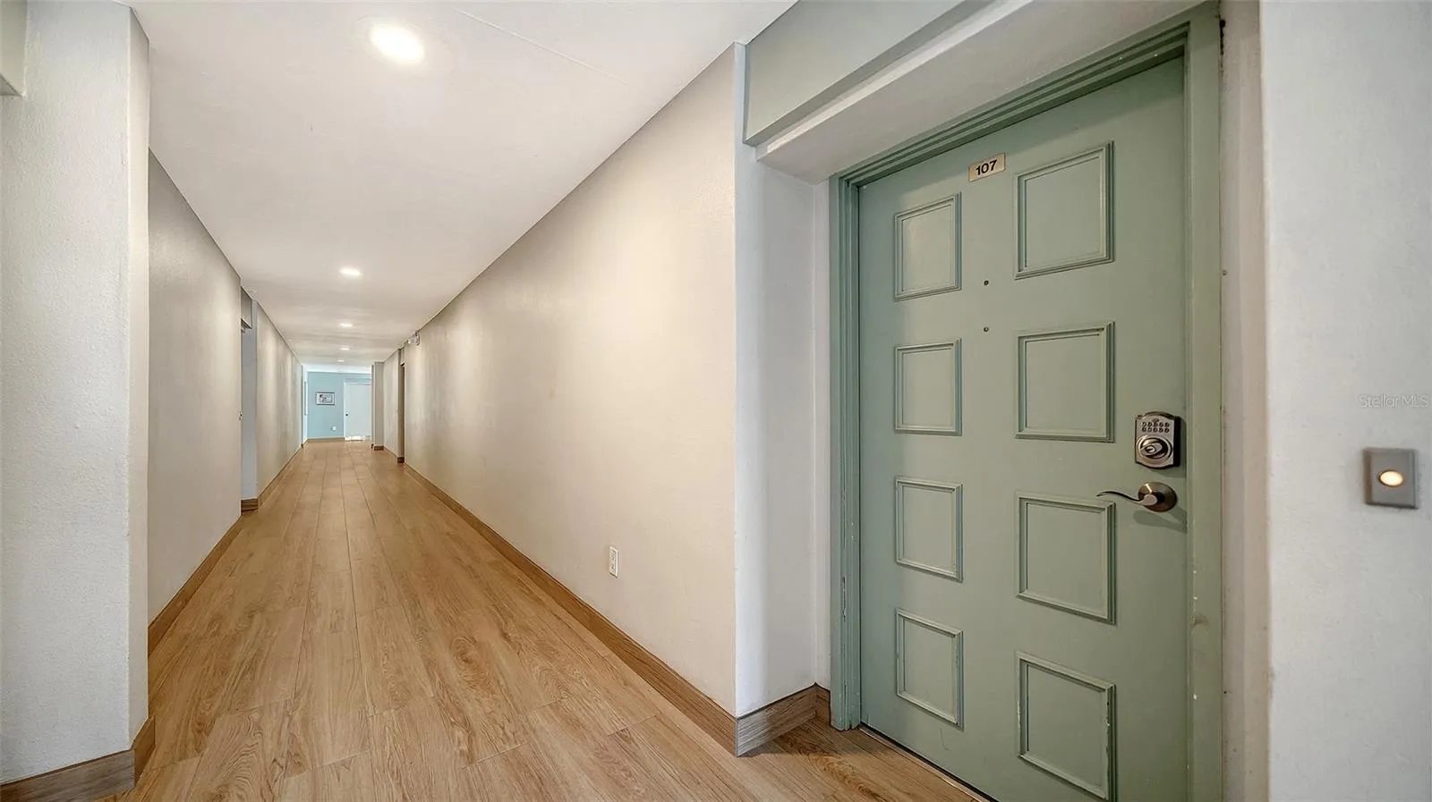 Front door of Unit #107.  Interior hallway of building features new 2025 tiled floors.