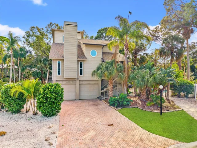 Elevated coastal-style home set on a quiet cul-de-sac with a paver driveway, oversized two-car garage, and lush tropical landscaping.